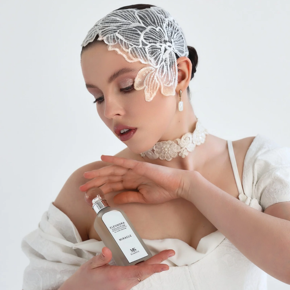 Woman in a white dress with lace headband holding a skincare bottle against a light background
